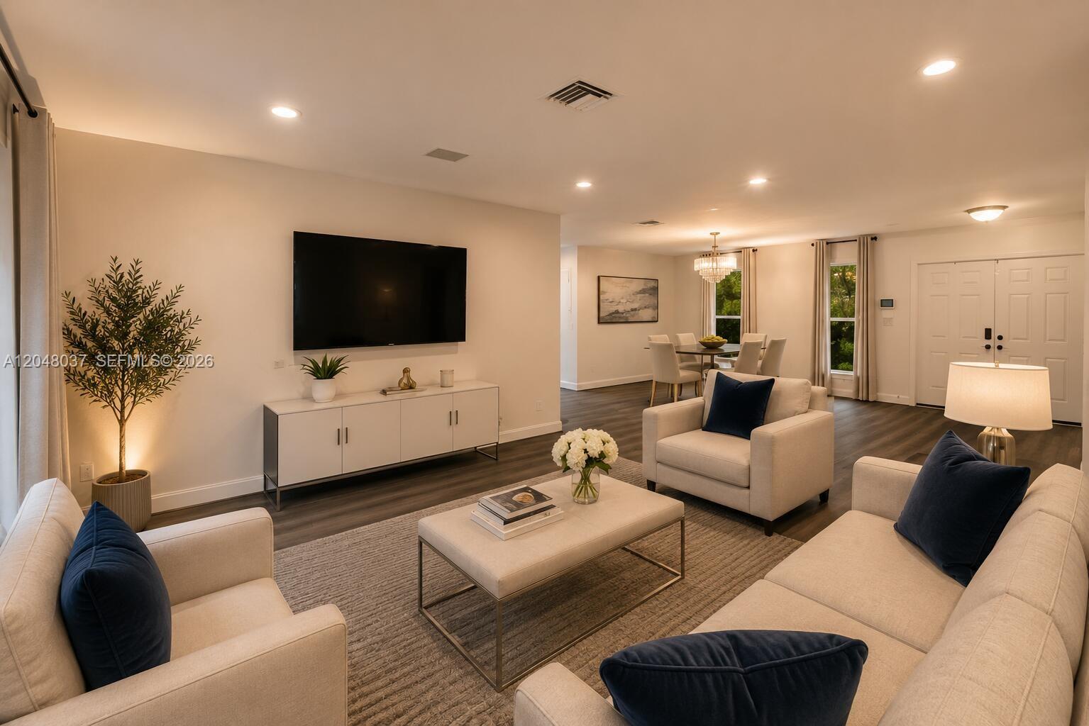 A modern living room features light-colored furniture, a large television, and dark wood flooring — 4740 N 31st Ct, Hollywood FL 33021, HOLLYWOOD, FL
