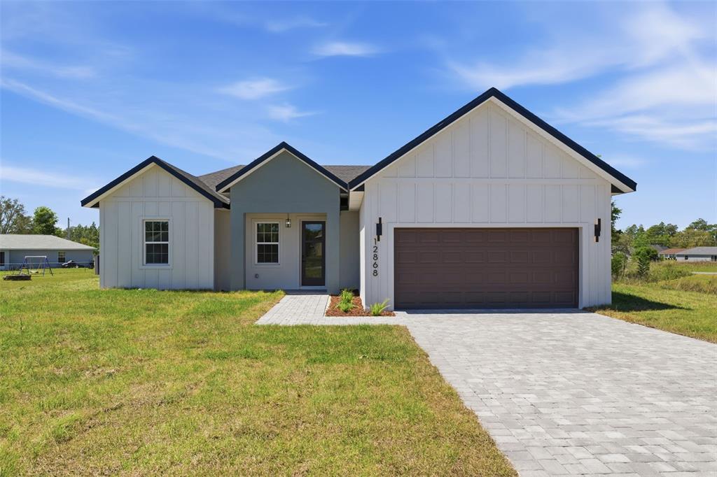 A modern single-story house features white board-and-batten siding, a gray entryway, and a brown garage — 12868 SW 73RD TERRACE, OCALA, FL