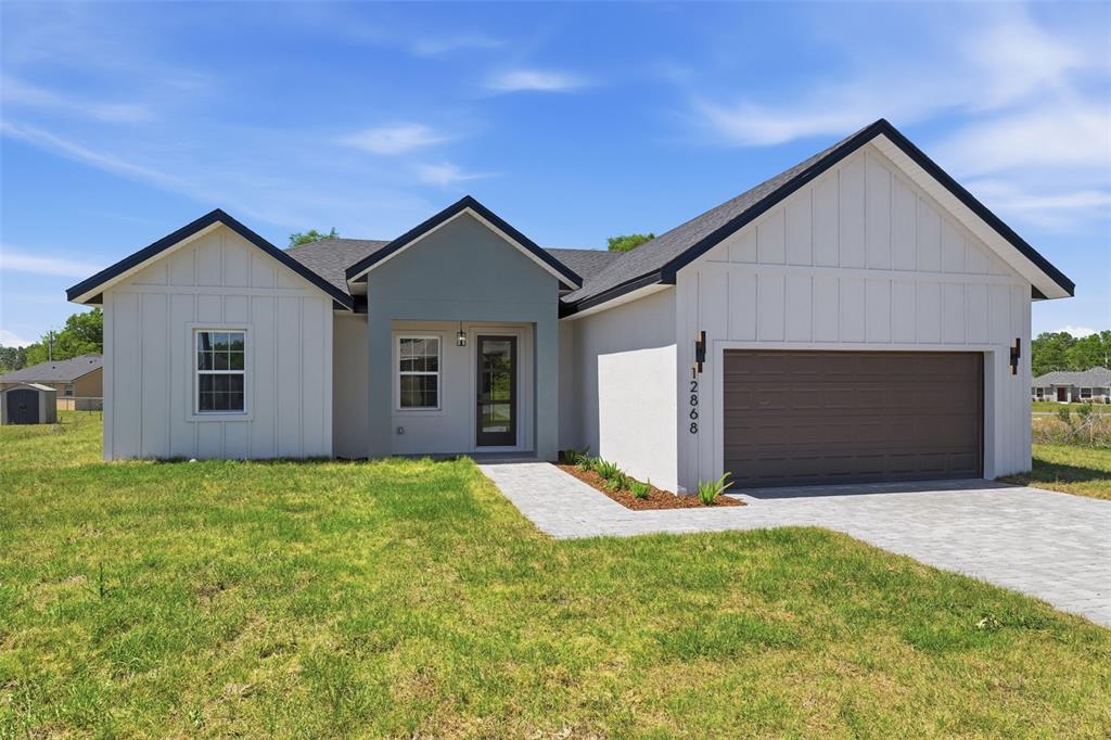A modern single-story house with white vertical siding, a gray entryway, and a two-car garage — 12868 SW 73RD TERRACE, OCALA, FL
