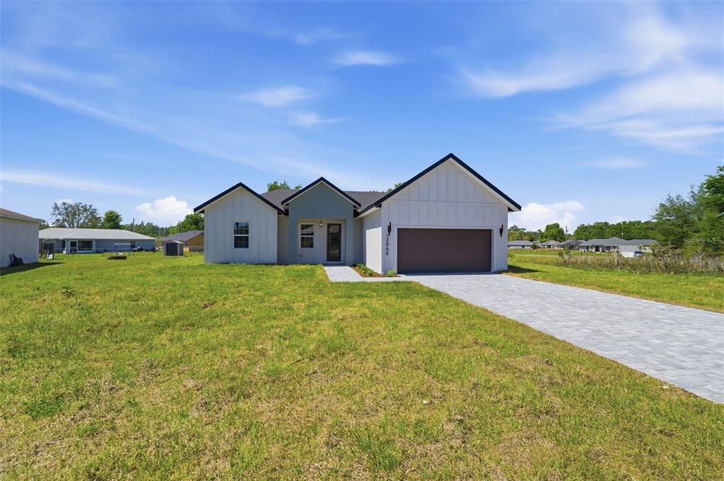 A single-story house with white board-and-batten siding, a dark garage door, and a paved driveway — 12868 SW 73RD TERRACE, OCALA, FL