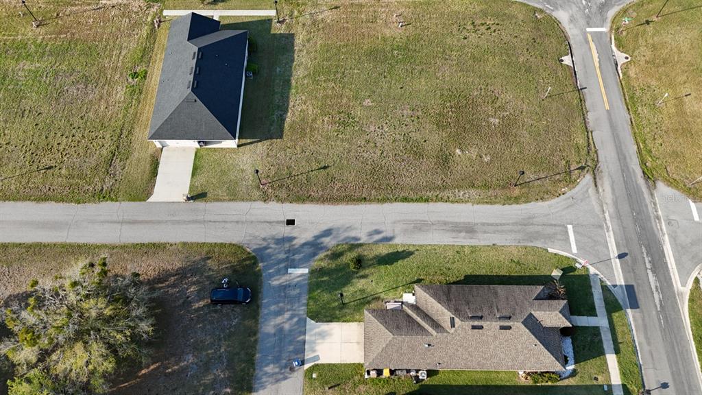 An aerial view shows two houses on a suburban street with a large grassy lot — 3100 ROCKY RIVER ROAD, KISSIMMEE, FL