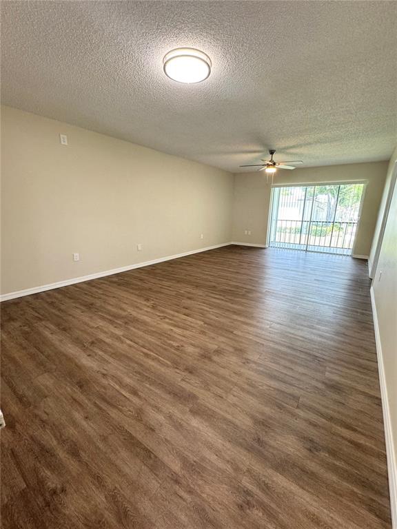An empty living room features wood-look flooring, a ceiling fan, and a sliding glass door — 134 CYPRESS COURT, OLDSMAR, FL