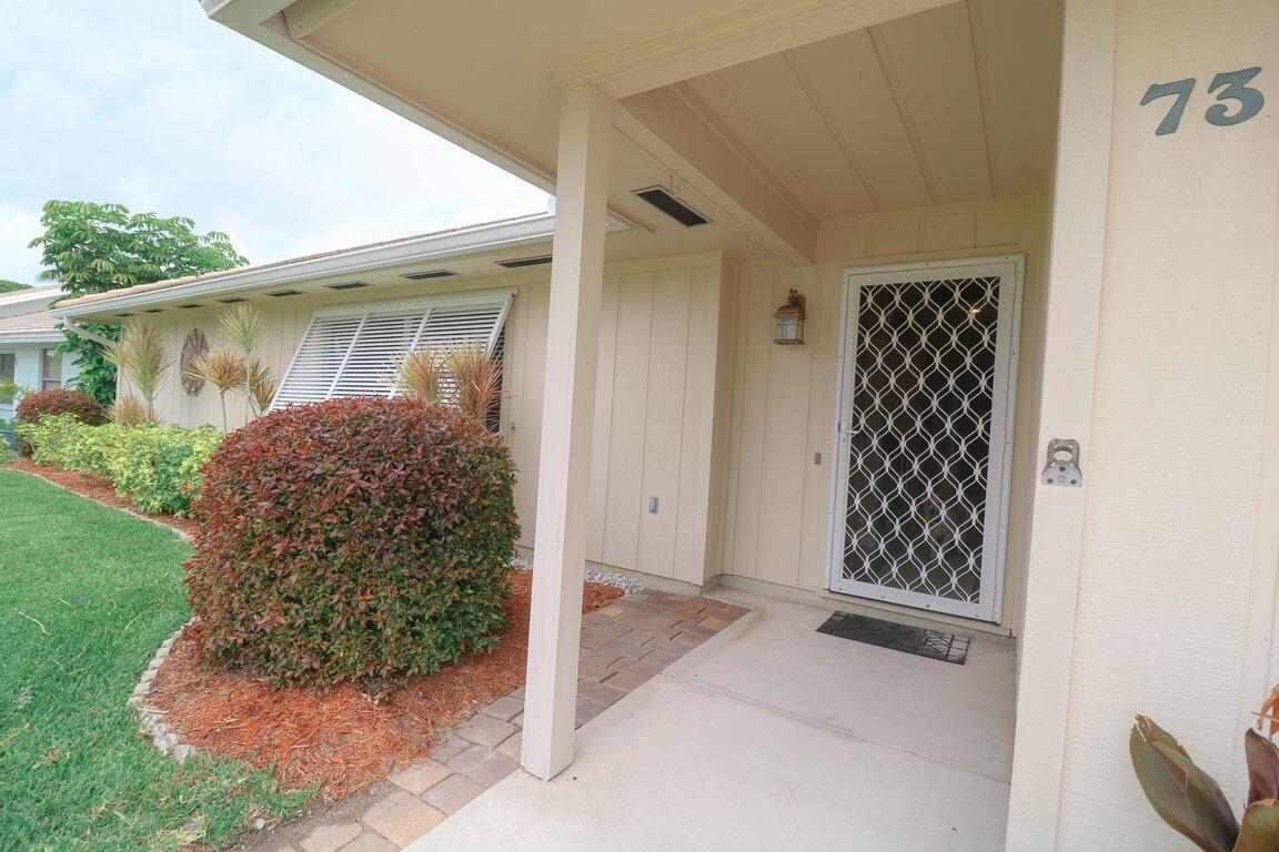 The exterior of a house features a covered entryway, a white security door, and landscaping — 73 Pine Hill Trail W, Jupiter FL 33469, JUPITER, FL