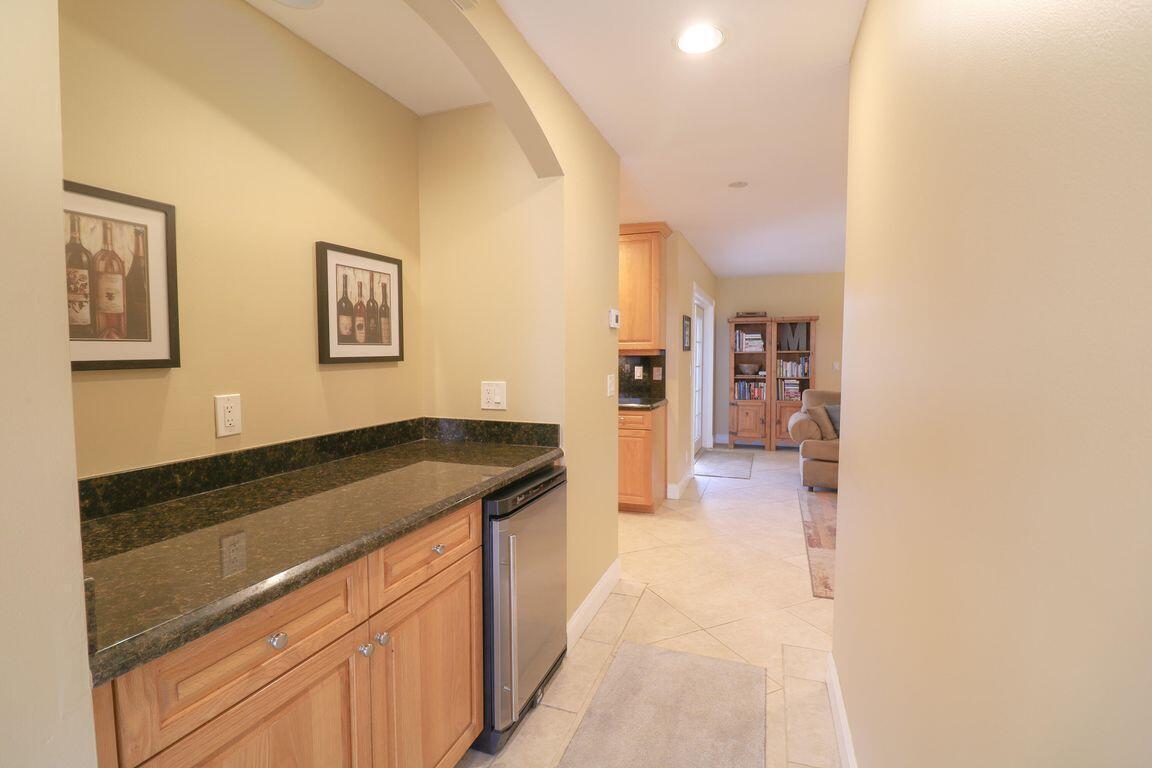 A wet bar with dark granite countertops and light wood cabinets sits in a hallway — 73 Pine Hill Trail W, Jupiter FL 33469, JUPITER, FL