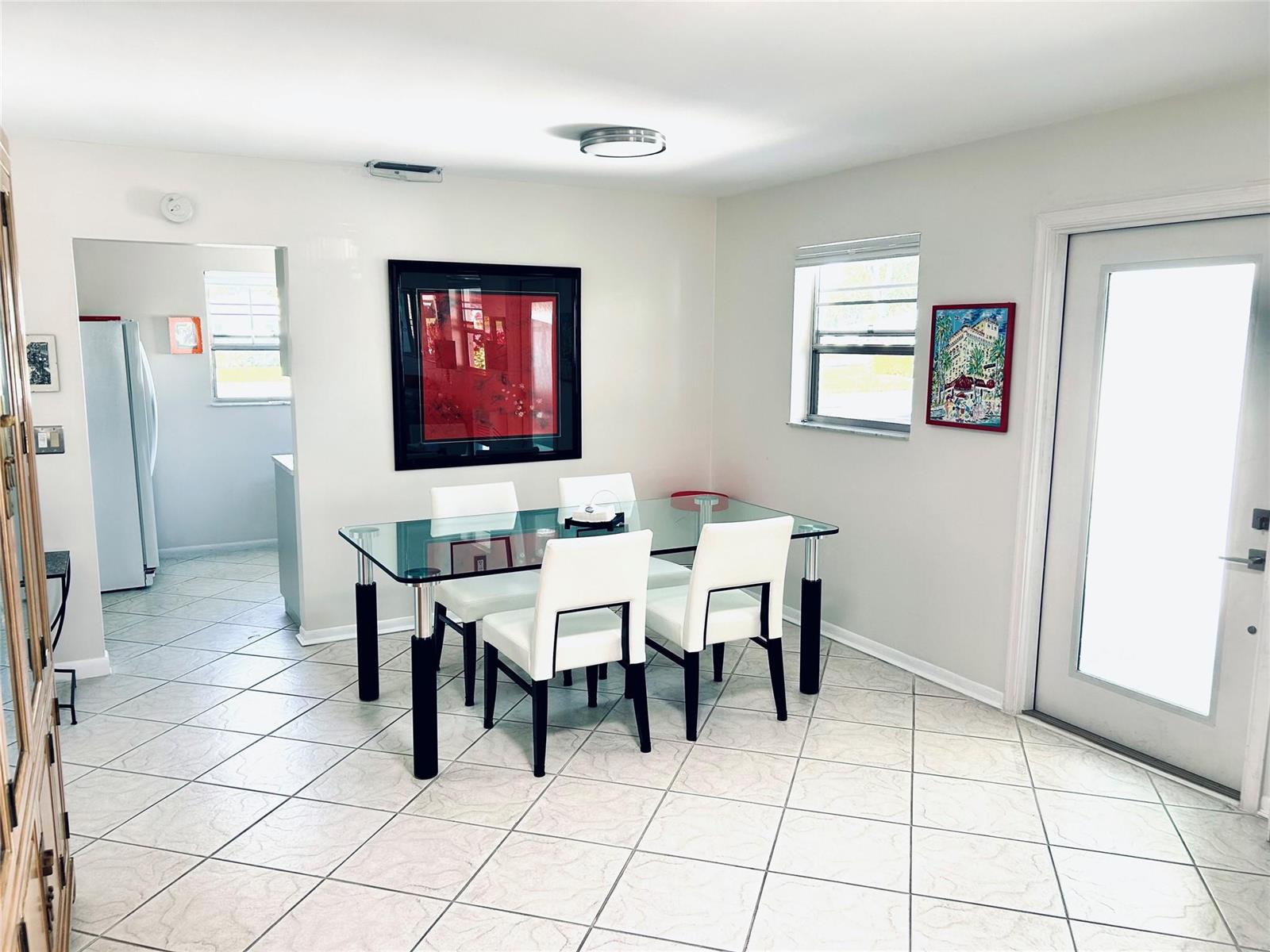 A dining room features a glass-top table, four white chairs, tile flooring, and wall art — 850 Meadowlark Lane, Delray Beach FL 33445, DELRAY BEACH, FL