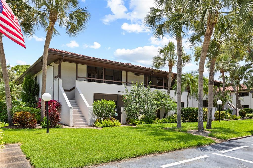 A two-story apartment building with a staircase, balcony, and palm trees on a sunny day — 3500 EL CONQUISTADOR PARKWAY UNIT 116, BRADENTON, FL