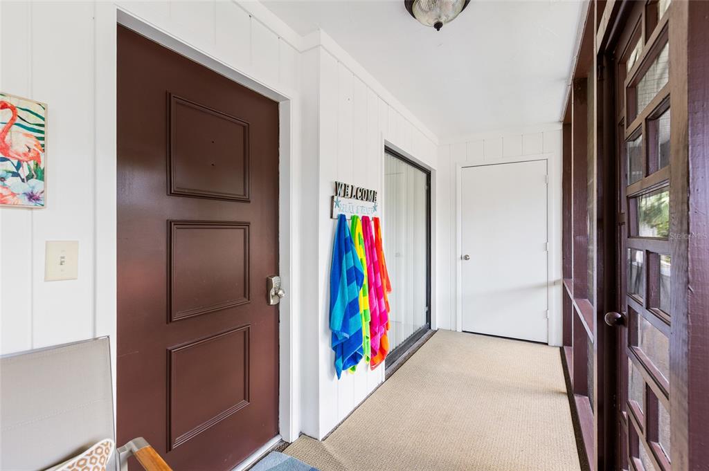 A covered porch features a brown door, white walls, and a row of colorful towels — 3500 EL CONQUISTADOR PARKWAY UNIT 116, BRADENTON, FL