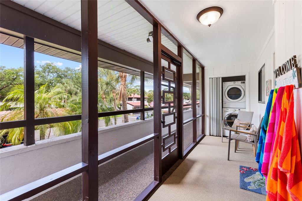 A screened-in balcony features a stacked washer and dryer, outdoor seating, and colorful hanging towels — 3500 EL CONQUISTADOR PARKWAY UNIT 116, BRADENTON, FL