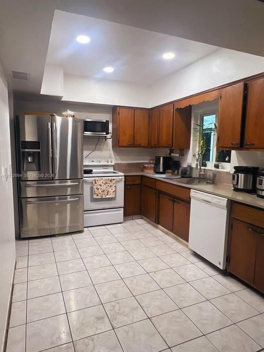 A kitchen features wood cabinets, stainless steel appliances, a white dishwasher, and tiled flooring — 6492 SW 25th St, Miramar FL 33023, MIRAMAR, FL