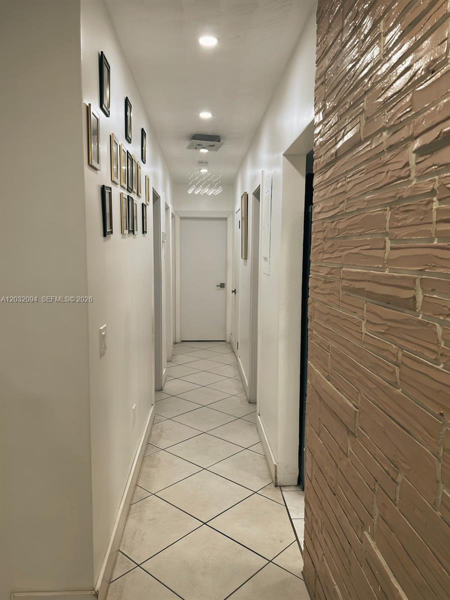 A narrow hallway features white walls, tiled floors, a textured accent wall, and framed photos — 6492 SW 25th St, Miramar FL 33023, MIRAMAR, FL