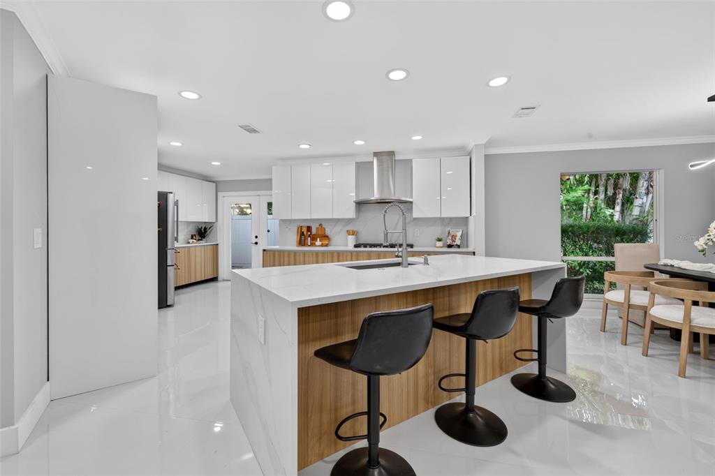 A modern kitchen features a large white quartz island, wood-toned cabinetry, and black bar stools — 219 MIRAMAR BOULEVARD NE, ST PETERSBURG, FL