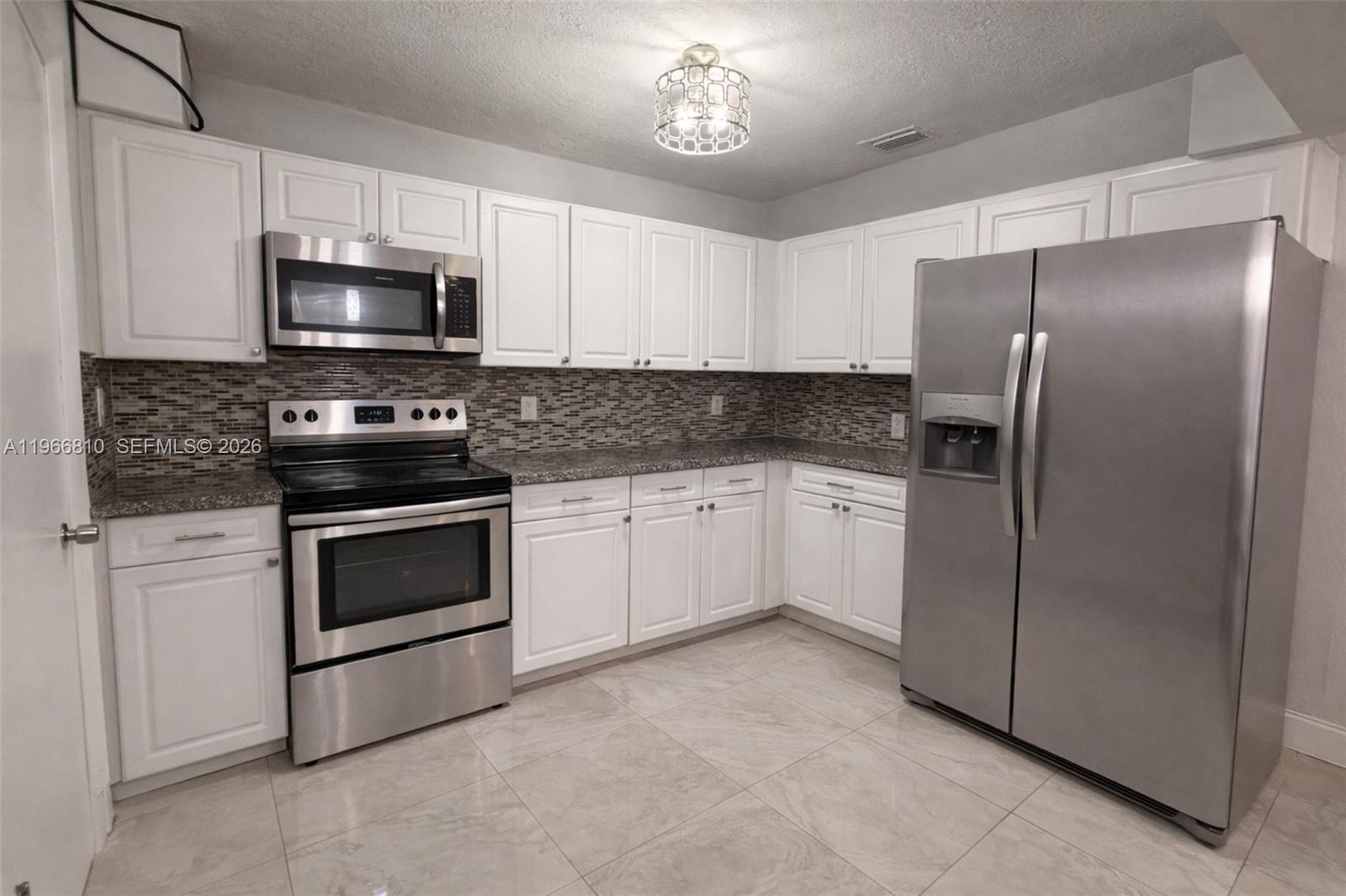 A kitchen features white cabinets, stainless steel appliances, granite countertops, and a tiled backsplash — 4500 NW 3rd Ave, Miami FL 33127, MIAMI, FL