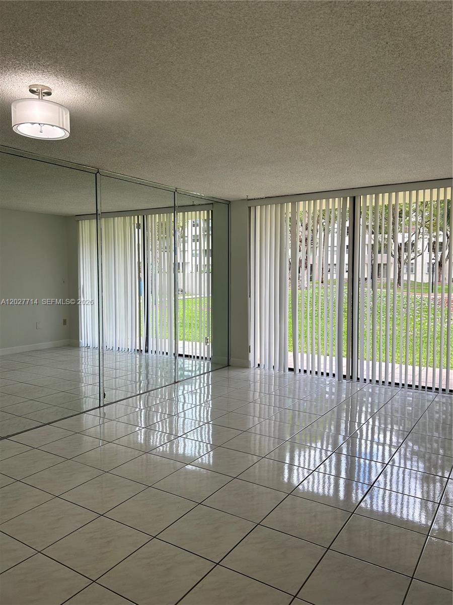An empty room features white tiled floors, a mirrored wall, and floor-to-ceiling vertical blinds — MIAMI, FL