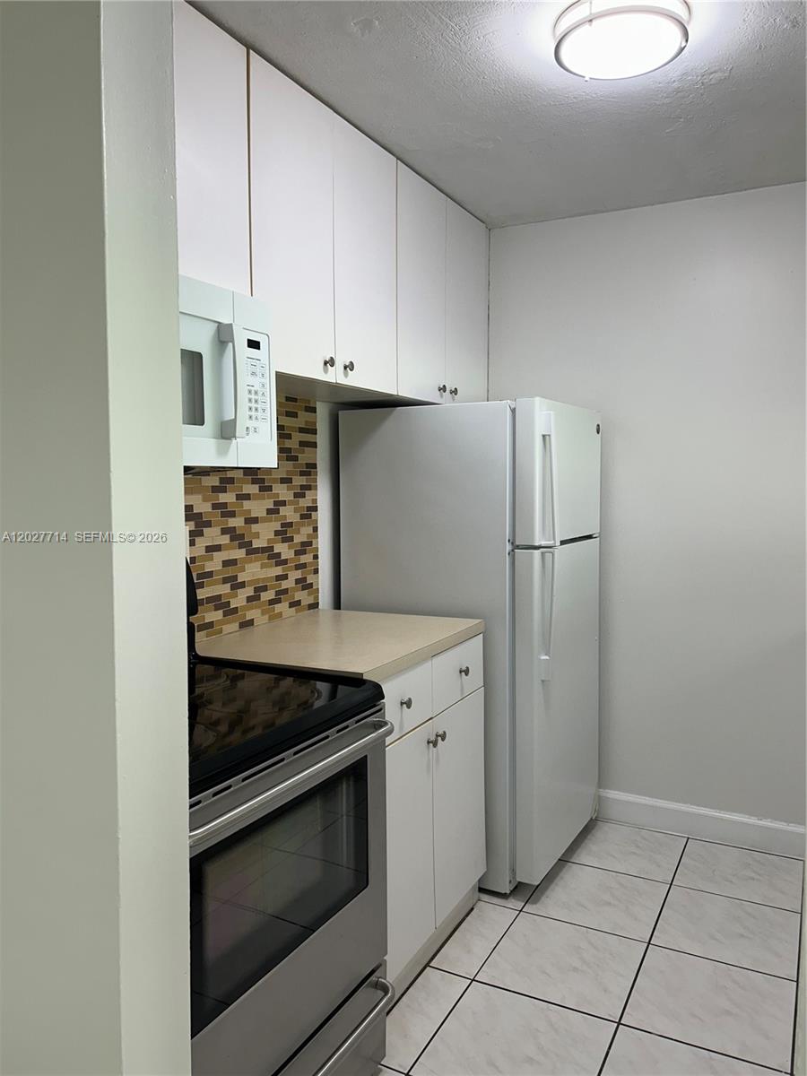 A kitchen features white cabinets, a stainless steel oven, a white refrigerator, and tiled floors — MIAMI, FL