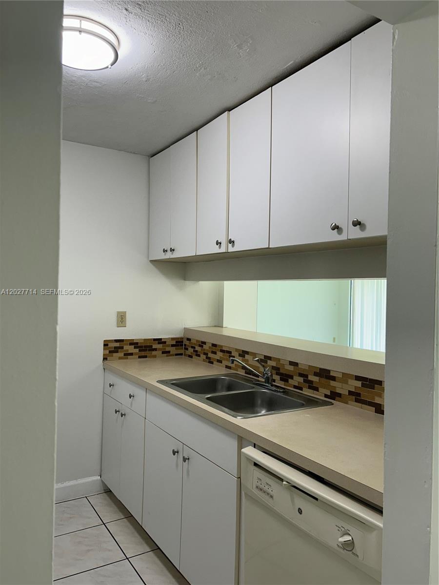 A kitchen features white cabinets, a beige countertop, a tiled backsplash, and a double sink — MIAMI, FL
