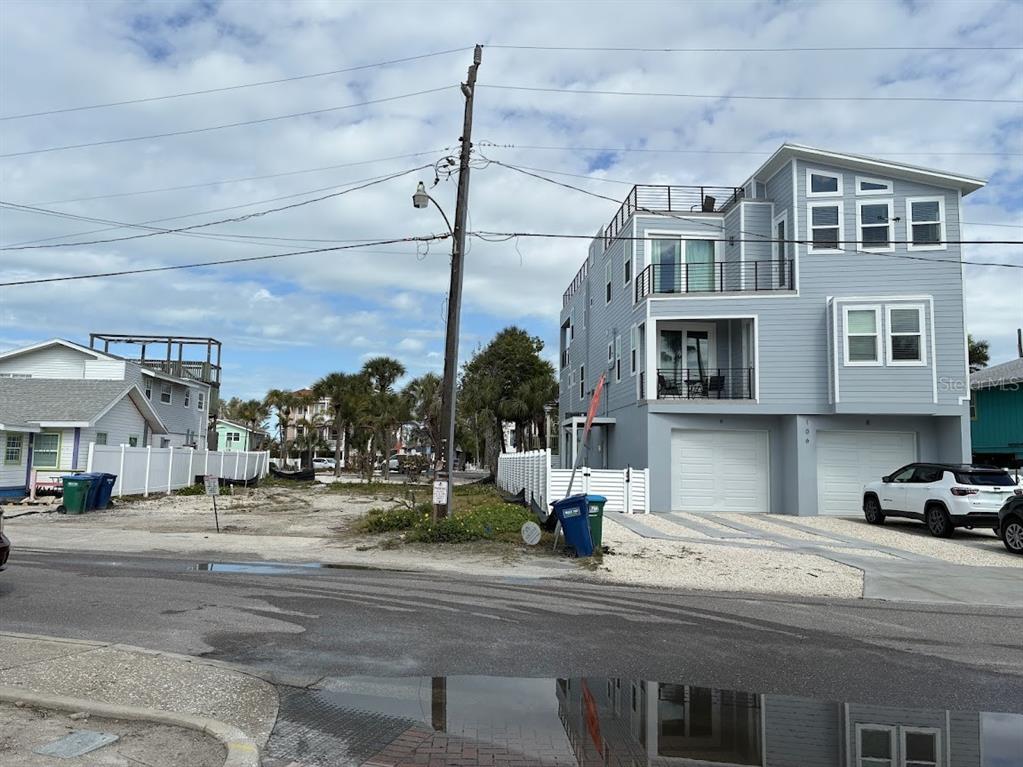 A modern three-story house stands next to a vacant lot on a paved street — 104 1ST STREET N, BRADENTON BEACH, FL