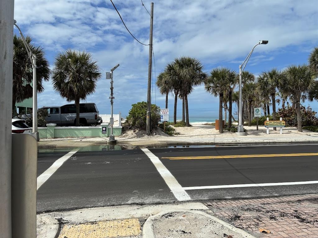 A street view shows a crosswalk leading to a sandy beach entrance with palm trees — 104 1ST STREET N, BRADENTON BEACH, FL