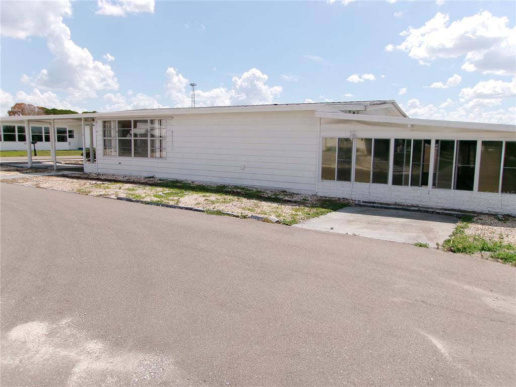 A white mobile home with a carport and an enclosed sunroom sits beside an asphalt road — 35055 DALE AVENUE, ZEPHYRHILLS, FL