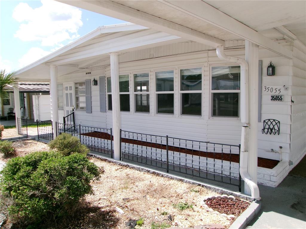 A white mobile home exterior features a covered porch, black metal railing, and large windows — 35055 DALE AVENUE, ZEPHYRHILLS, FL
