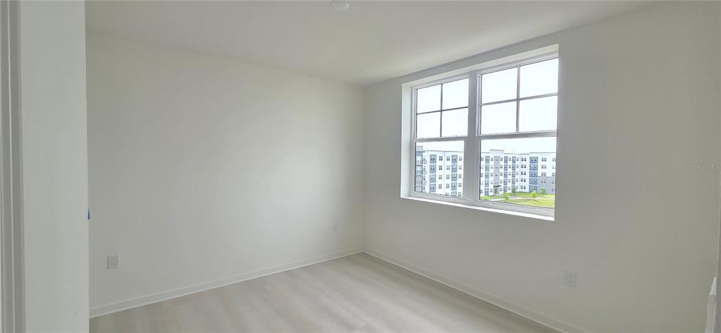 An empty room with white walls, light wood-look flooring, and a large window — 5579 MILLENIA PARK BOULEVARD UNIT 503, ORLANDO, FL