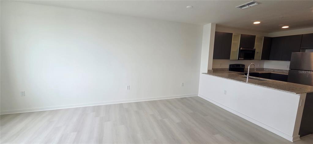 An open-concept living area features light wood-look flooring and a kitchen with dark cabinetry — 5579 MILLENIA PARK BOULEVARD UNIT 503, ORLANDO, FL