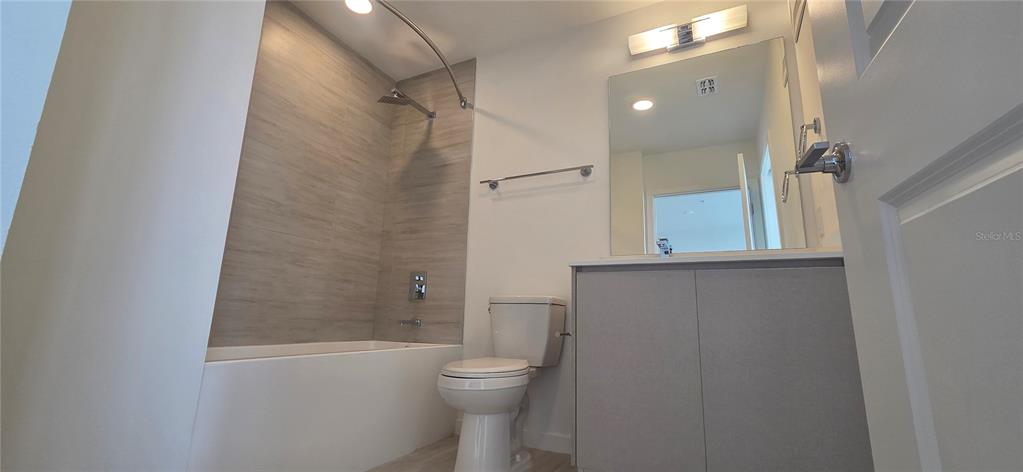 A bathroom features a bathtub with tiled walls, a toilet, and a vanity with mirror — 5579 MILLENIA PARK BOULEVARD UNIT 503, ORLANDO, FL