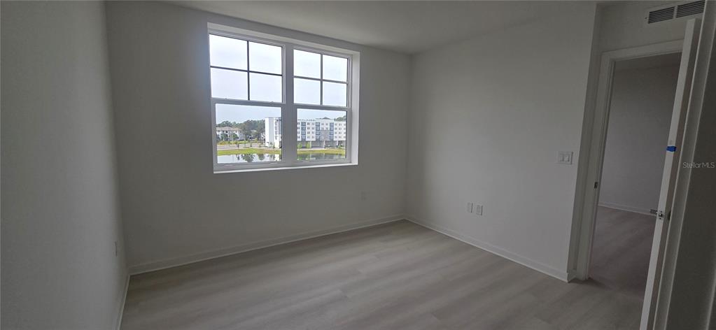 An empty bedroom with white walls, light wood-look flooring, and a window overlooking a pond — 5579 MILLENIA PARK BOULEVARD UNIT 503, ORLANDO, FL