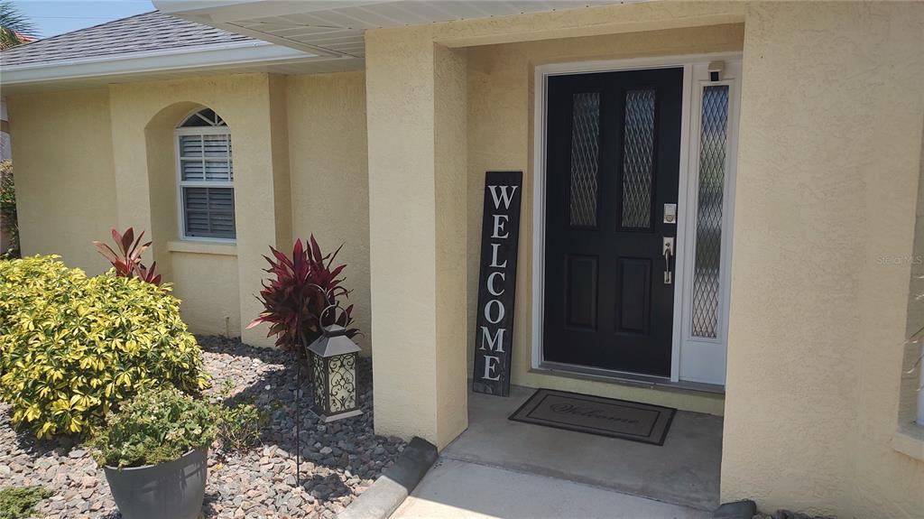 A black front door with a side light and a vertical welcome sign on a porch — 4835 JACARANDA HEIGHTS DRIVE, VENICE, FL