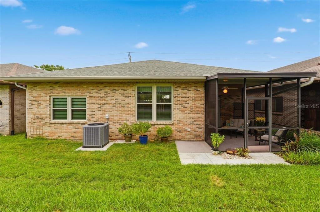 The back exterior of a brick house features a screened-in patio and a grass lawn — 730 MARTINIQUE CIRCLE, LAKELAND, FL