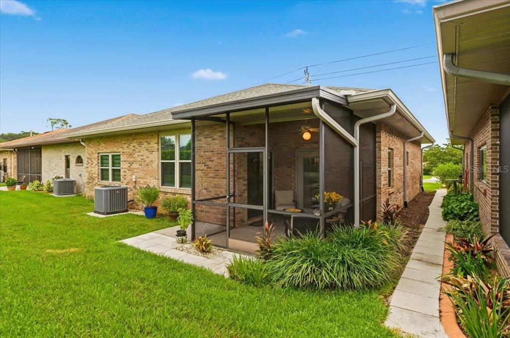A brick house exterior features a screened-in porch, a grassy lawn, and a paved walkway — 730 MARTINIQUE CIRCLE, LAKELAND, FL