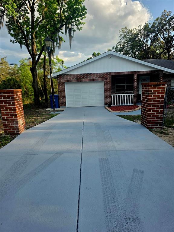 A single-story brick house features a white garage door and a freshly painted gray driveway — 8088 CLIPPER COURT, SPRING HILL, FL