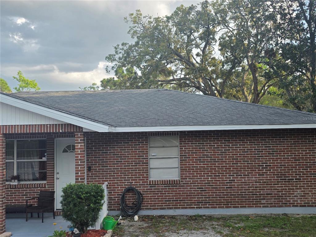A brick house exterior features a gray shingled roof, a white door, and a window — 8088 CLIPPER COURT, SPRING HILL, FL