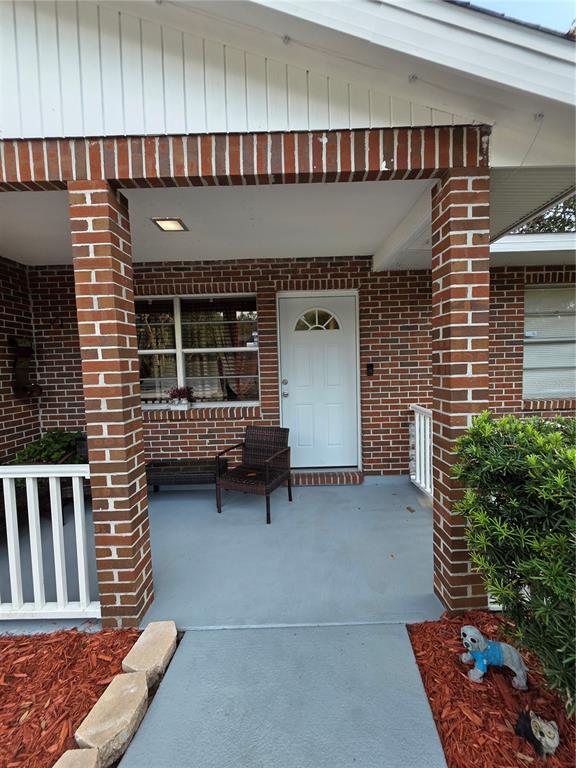 A brick-front house features a covered porch with a white door and a gray floor — 8088 CLIPPER COURT, SPRING HILL, FL