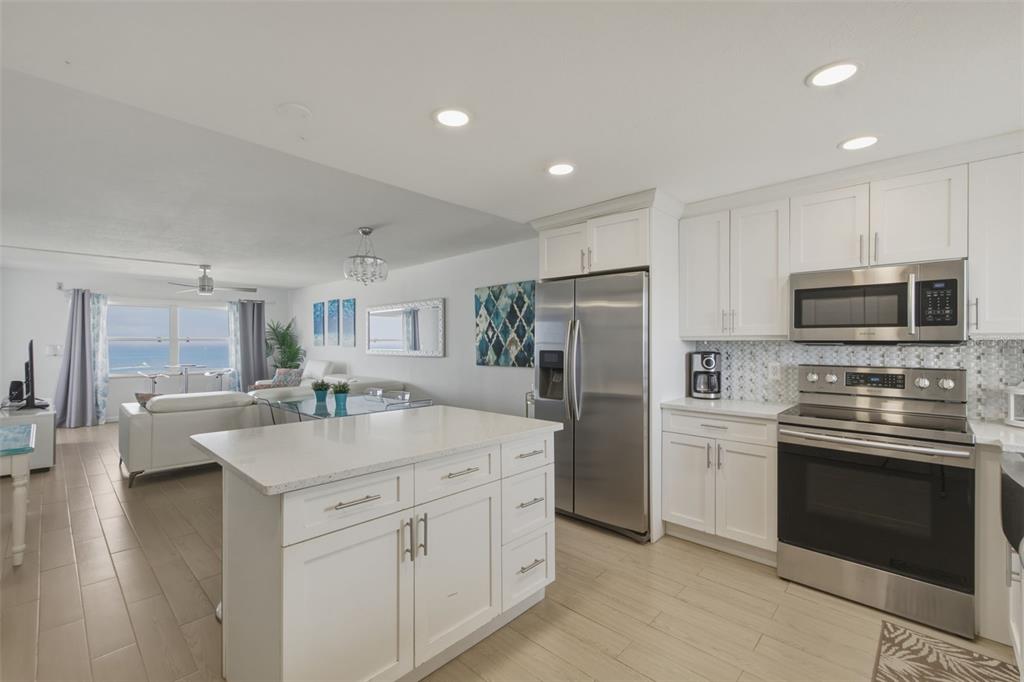 A modern kitchen with white cabinets and stainless steel appliances overlooks a living area — 1270 GULF BOULEVARD UNIT 1202, CLEARWATER BEACH, FL