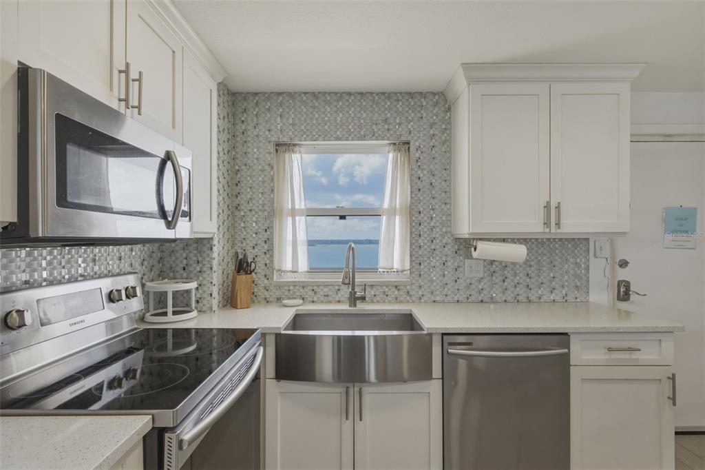 A kitchen features white cabinets, stainless steel appliances, a farmhouse sink, and a water view — 1270 GULF BOULEVARD UNIT 1202, CLEARWATER BEACH, FL
