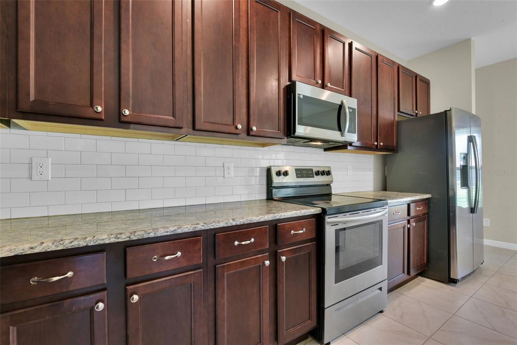 A kitchen features dark wood cabinets, stainless steel appliances, granite countertops, and a white backsplash — 25599 DEEP CREEK BOULEVARD, PUNTA GORDA, FL
