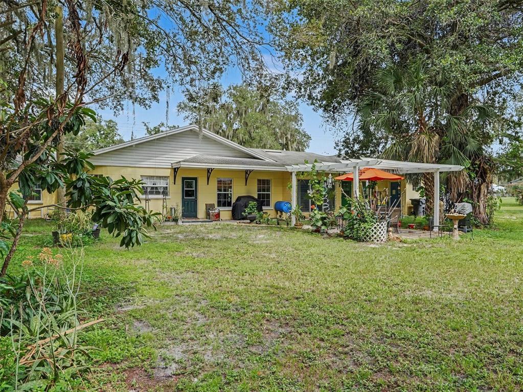 A yellow single-story house features a white pergola over a patio in a grassy yard — 3300 BAILEY ROAD, MULBERRY, FL