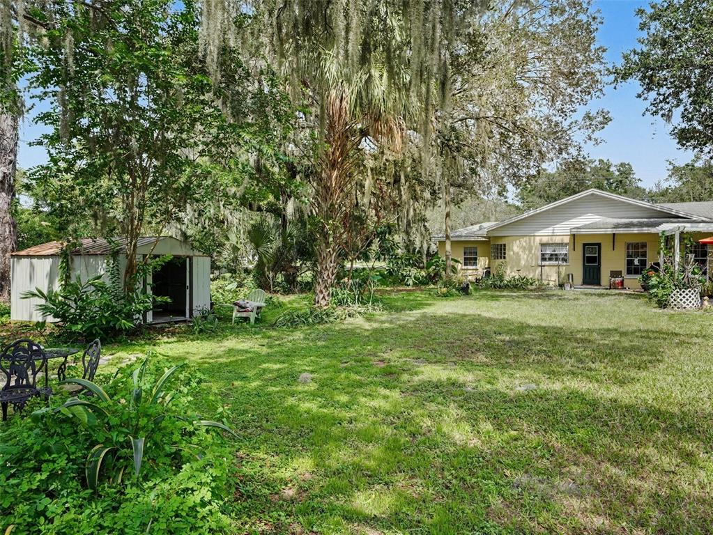 A backyard features a metal storage shed, a yellow house, and large trees with Spanish moss — 3300 BAILEY ROAD, MULBERRY, FL