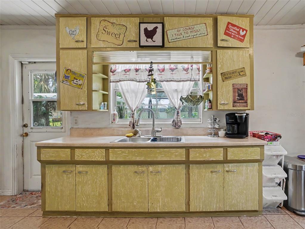 A kitchen features yellow distressed cabinets, a double sink, and a window with rooster-themed curtains — 3300 BAILEY ROAD, MULBERRY, FL