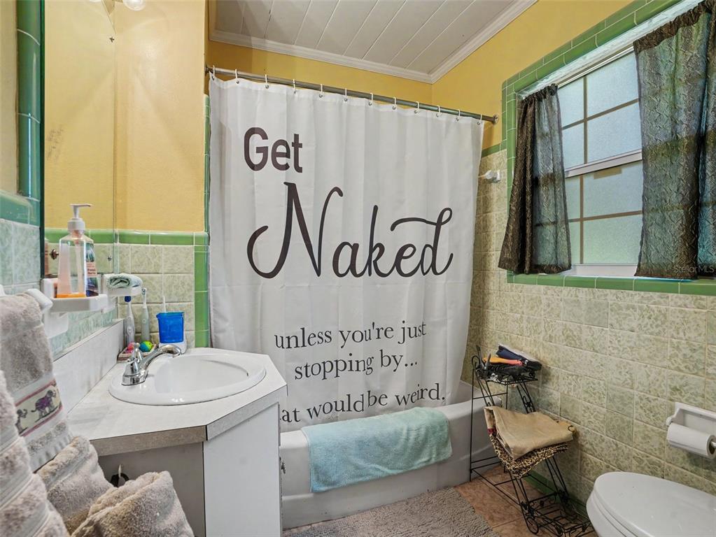 A bathroom features green tile, a white vanity, and a shower curtain with text — 3300 BAILEY ROAD, MULBERRY, FL