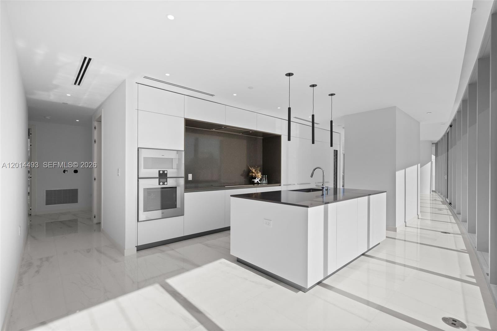 A modern kitchen features white cabinetry, a dark stone island, and polished marble flooring — 300 Biscayne Blvd Way # 3801, Miami FL 33131, MIAMI, FL