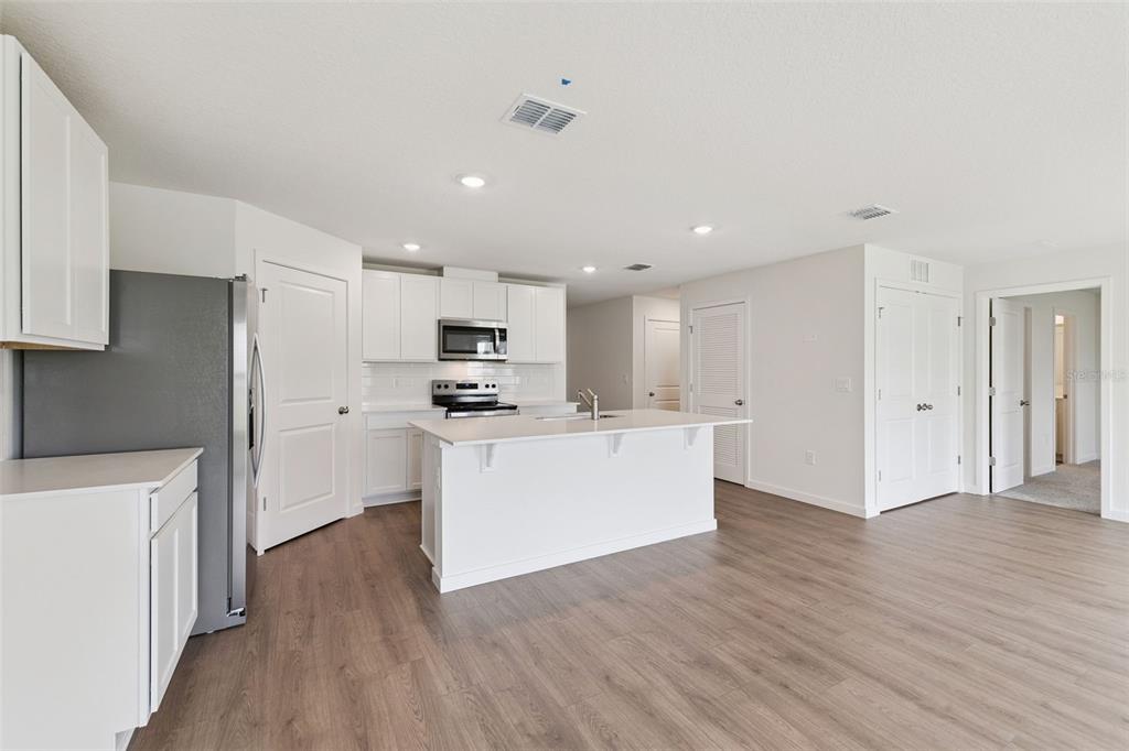 A modern kitchen features white cabinetry, stainless steel appliances, a center island, and wood-look flooring — 904 E MICHIGAN AVENUE, DELAND, FL