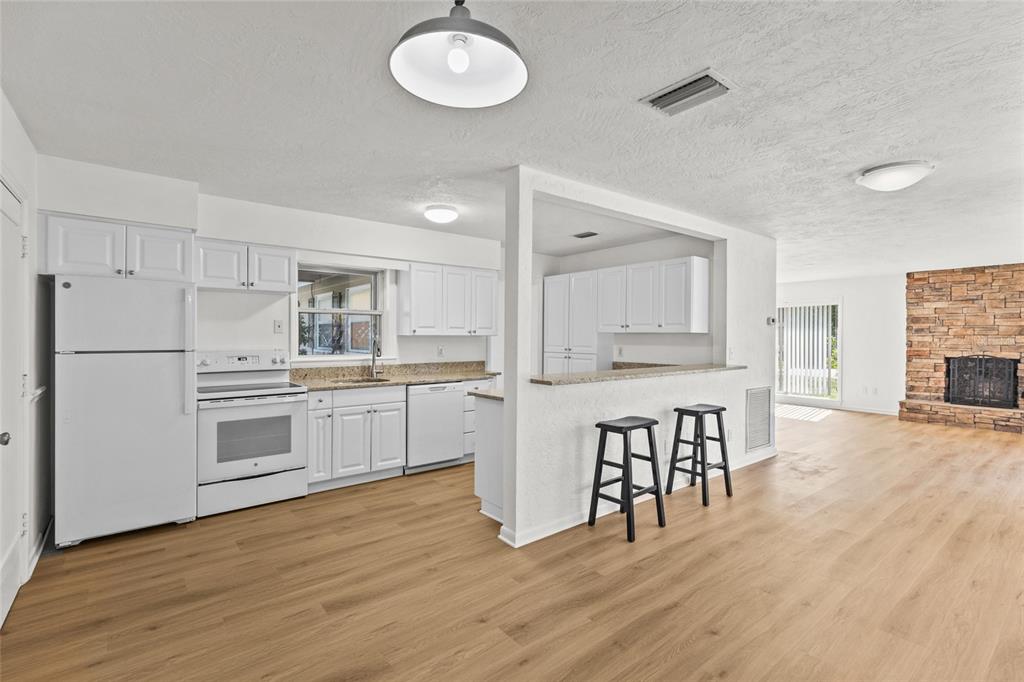 A white kitchen with a breakfast bar overlooks a living area featuring a stone fireplace — 2588 COLORADO STREET, SARASOTA, FL