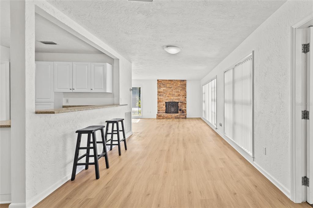 A living room with light wood flooring, a stone fireplace, and a kitchen breakfast bar — 2588 COLORADO STREET, SARASOTA, FL