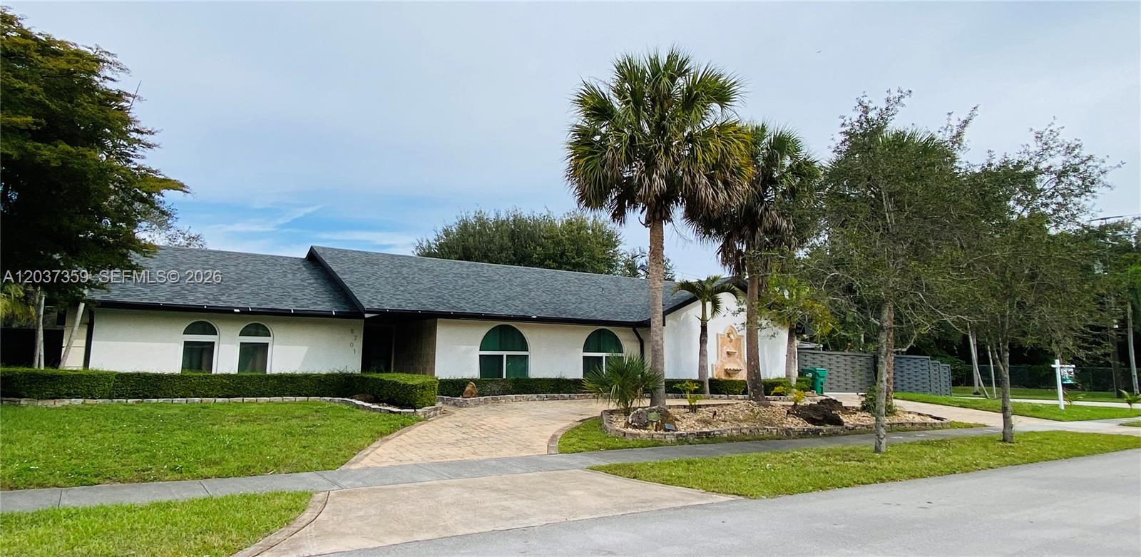A single-story white house with a dark shingled roof and arched windows sits behind landscaping — 8701 SW 191st St, Cutler Bay FL 33157, CUTLER BAY, FL