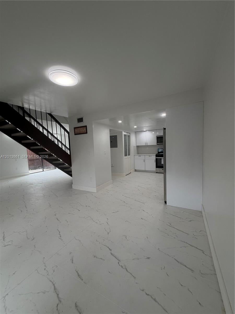 This interior view shows a kitchen with white cabinets, marble-look tile flooring, and a staircase — 7024 SW 114th Pl # 52, Miami FL 33173, MIAMI, FL