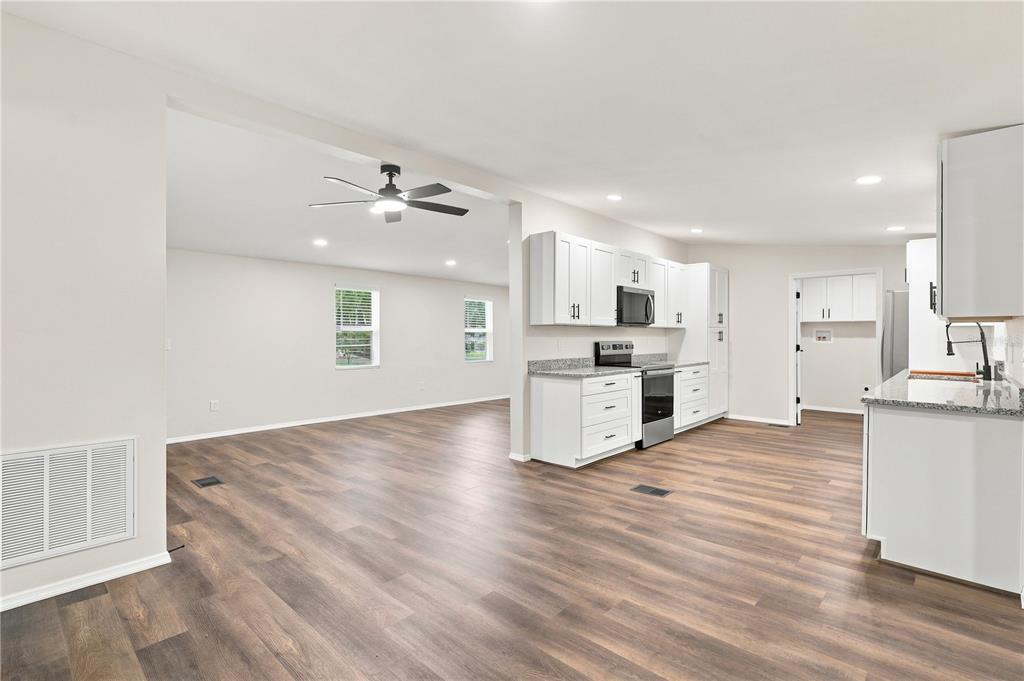 An open-concept kitchen and living area featuring white cabinets, granite countertops, and wood-look flooring — 16918 SUGAR BERRY LANE, MONTVERDE, FL