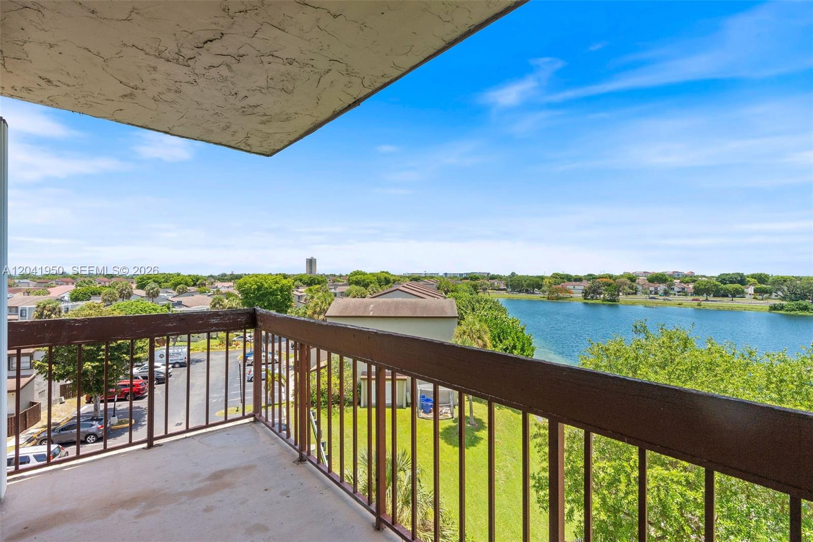 A balcony with a brown metal railing overlooks a parking lot, green space, and lake — 10288 NW 9th St Cir # 501, Miami FL 33172, MIAMI, FL
