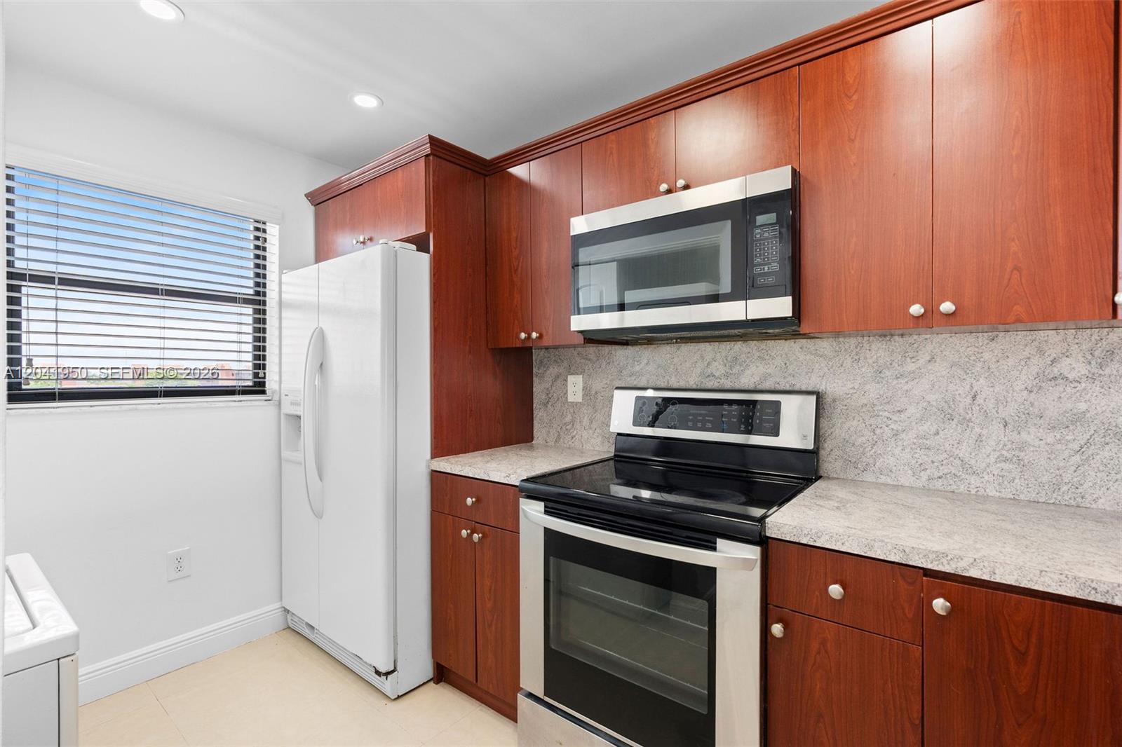 A kitchen features cherry-toned wood cabinets, stainless steel appliances, and light-colored granite countertops — 10288 NW 9th St Cir # 501, Miami FL 33172, MIAMI, FL