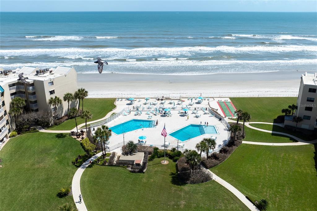 An aerial view shows a beachfront resort with two swimming pools and surrounding green lawns — 4501 S ATLANTIC AVENUE UNIT 209, NEW SMYRNA BEACH, FL